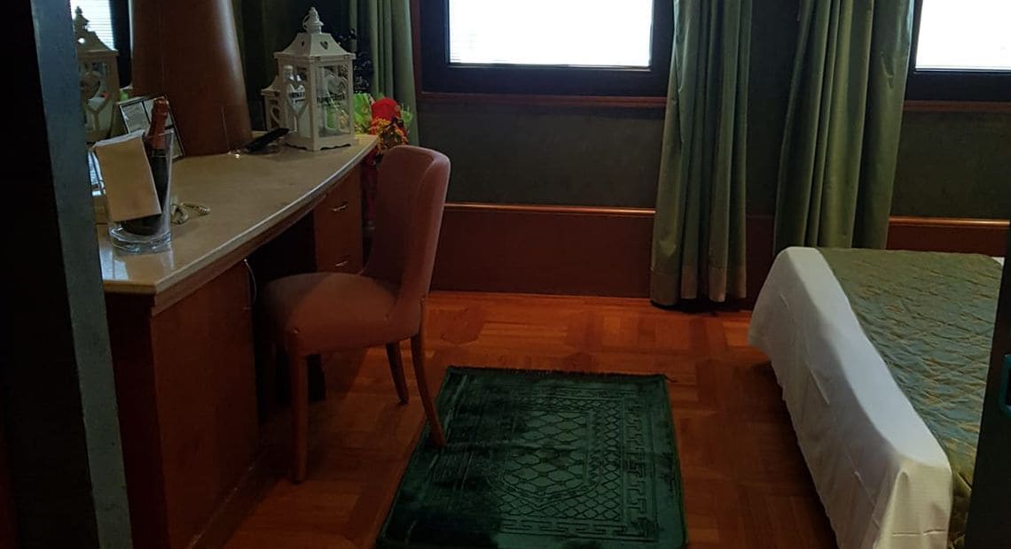 A room with a desk, chair, bed, and a green rug.