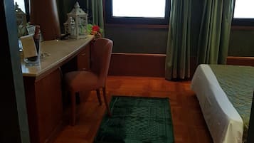 A room with a desk, chair, bed, and a green rug.