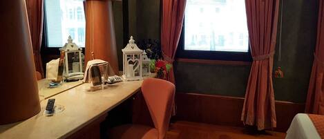 A hotel room with a wooden desk, a chair, a bed, and a window with curtains.