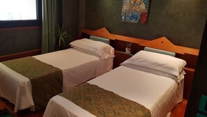 A hotel room with two single beds, a wooden headboard, a small table with a vase, and a painting on the wall. - HR Hotel (Monfalcone)