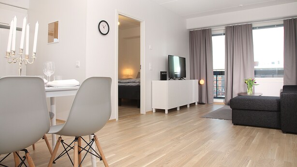 A modern living room with a dining area, a television, and a balcony with curtains. - DP Apartments Vaasa (Vaasa)