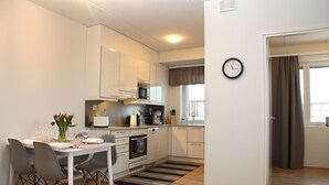 A modern kitchen with white cabinets, a microwave, and a dining area with a table set for four. - DP Apartments Vaasa (Vaasa)