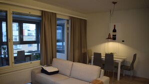 A modern living room with a sofa, dining table, chairs, and a window with curtains. - DP Apartments Vaasa (Vaasa)