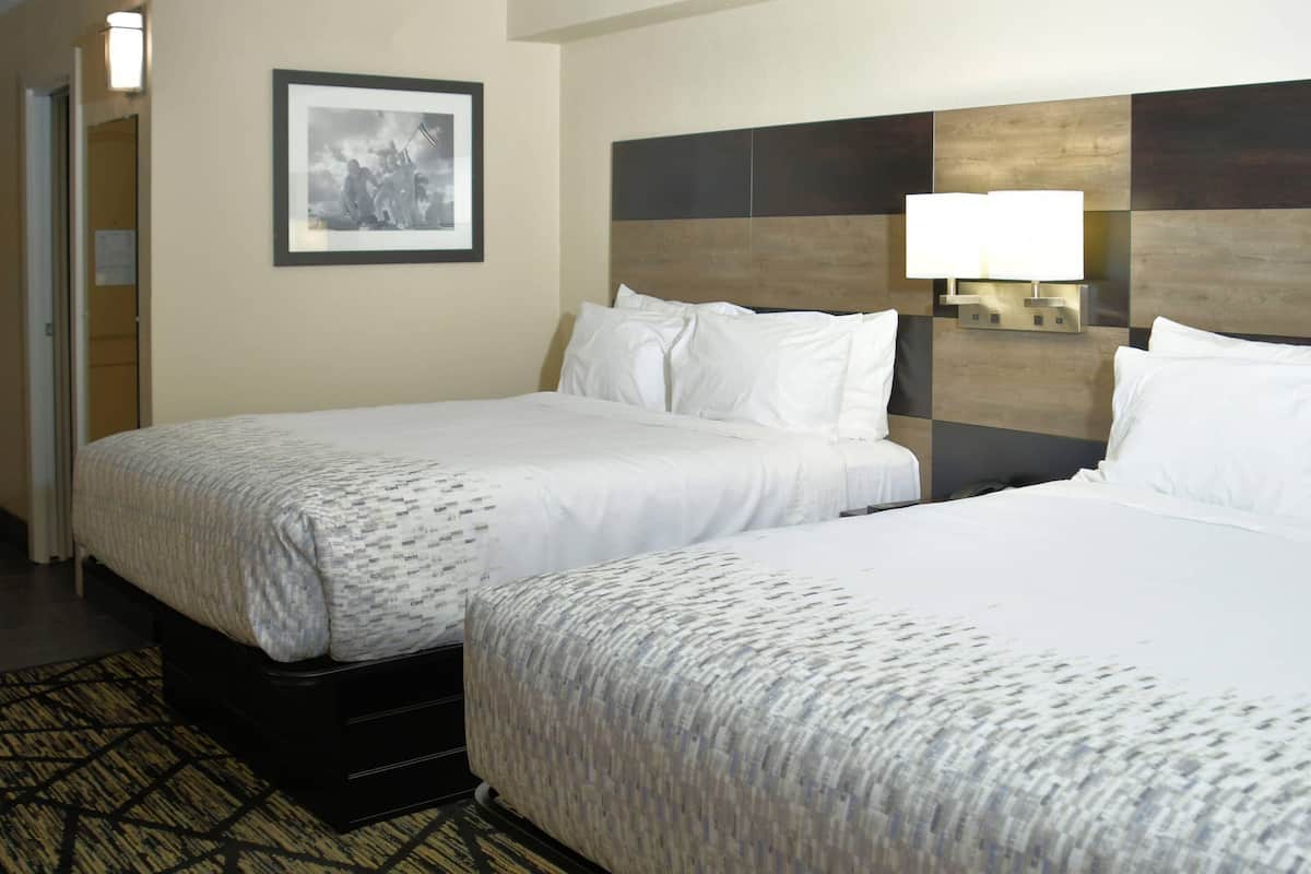A hotel room with two beds, a framed picture on the wall, and a nightstand with a lamp.