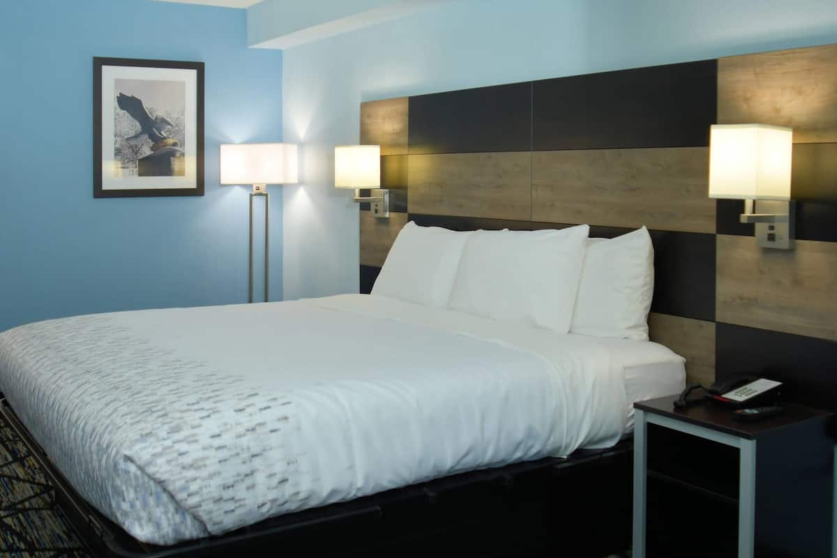 A hotel room with a large bed, two bedside lamps, a framed picture on the wall, and a nightstand with a phone.