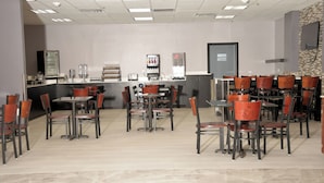 A restaurant with multiple tables and chairs, a counter with a cash register, and a wall-mounted television.