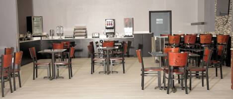 A restaurant with multiple tables and chairs, a counter with a cash register, and a wall-mounted television.