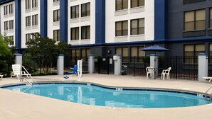A hotel exterior with a swimming pool, outdoor seating, and a gated entrance.