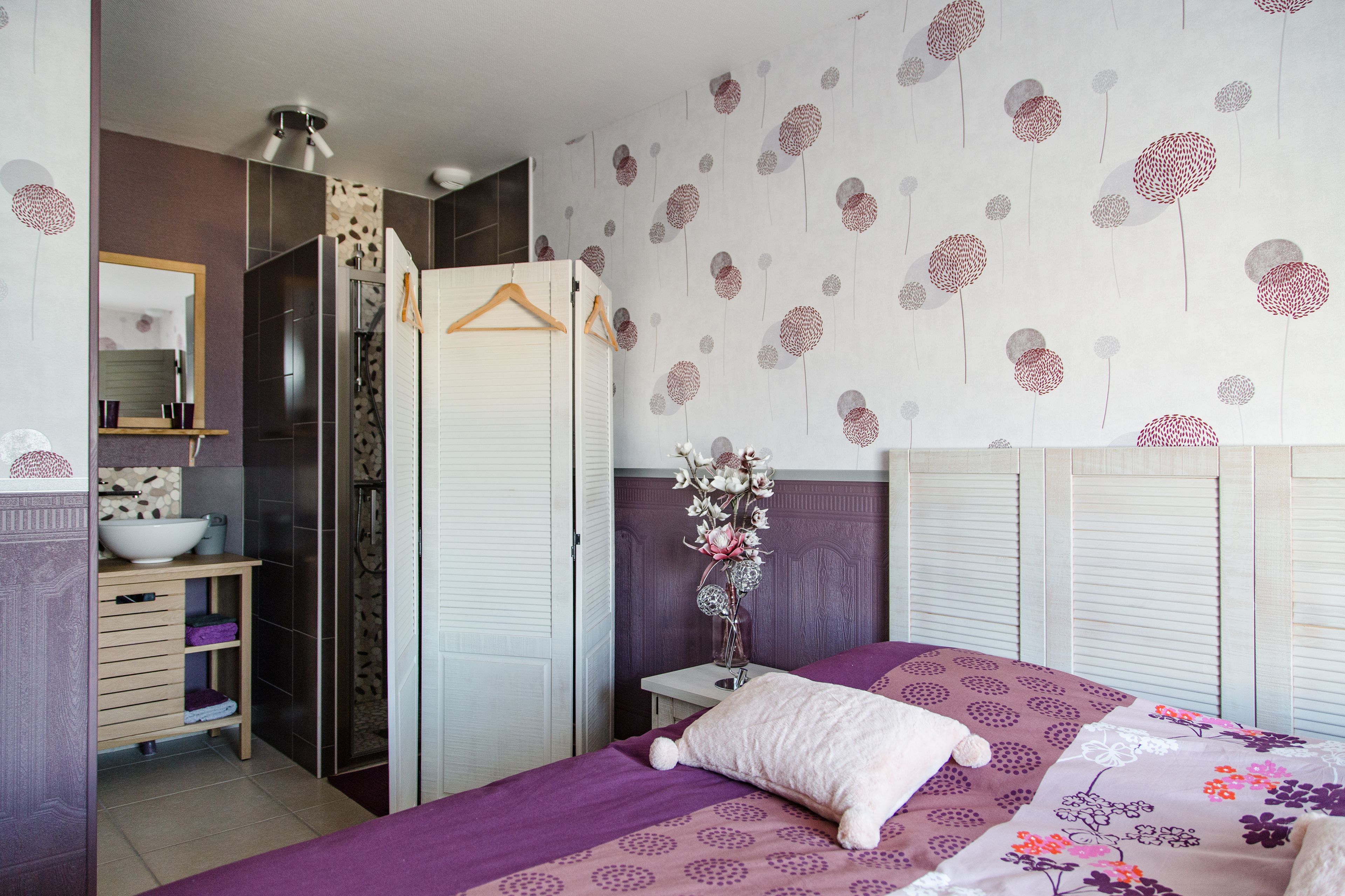 Un dormitorio con cama, armario, espejo y baño con ducha.