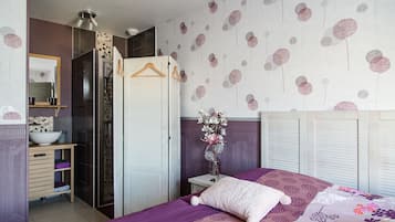 Un dormitorio con cama, armario, espejo y baño con ducha.