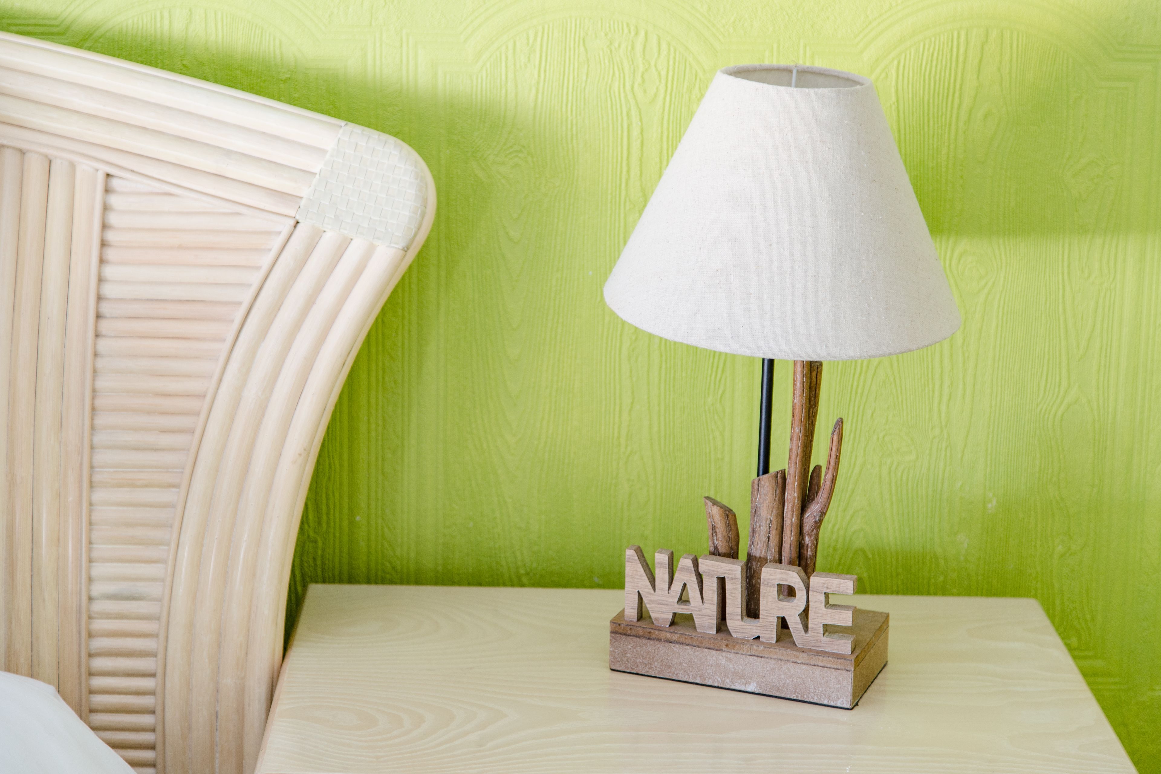 Une table de chevet en bois, sur laquelle se trouve une lampe blanche et un bloc portant le mot « NATURE ».