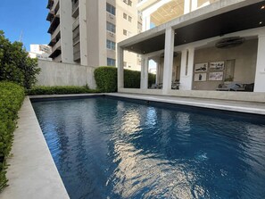 A swimming pool with a clear blue water surface, surrounded by a low concrete wall and green hedges. - Stay At Mare (San Juan)