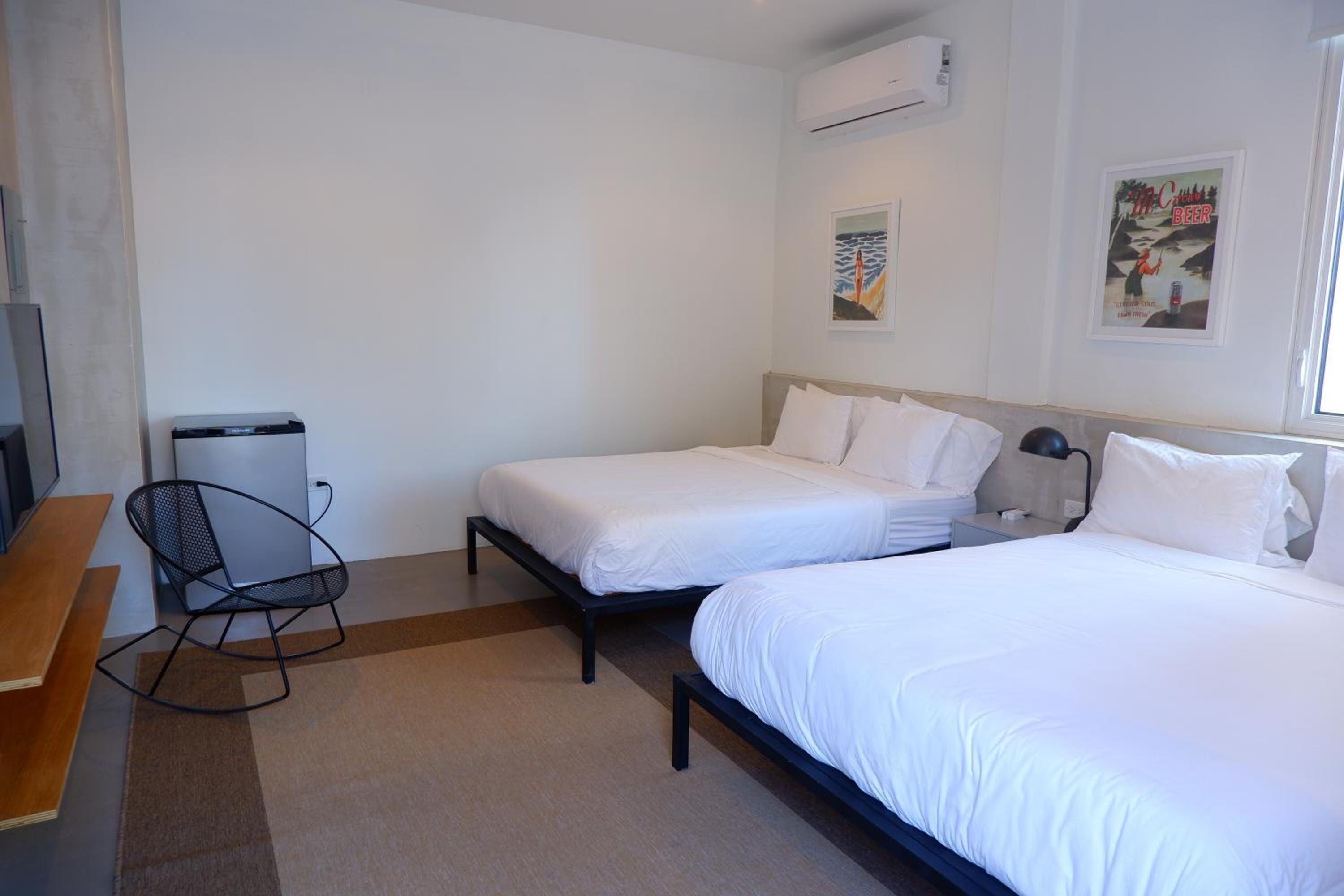Une chambre d’hôtel avec deux lits simples, un bureau, une chaise et une poubelle.