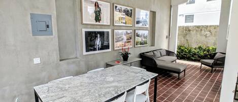 Une cuisine moderne avec un plan de travail en marbre, des chaises blanches et une table à manger. Des tableaux encadrés ornent le mur, et un ventilateur de plafond est installé au plafond.
