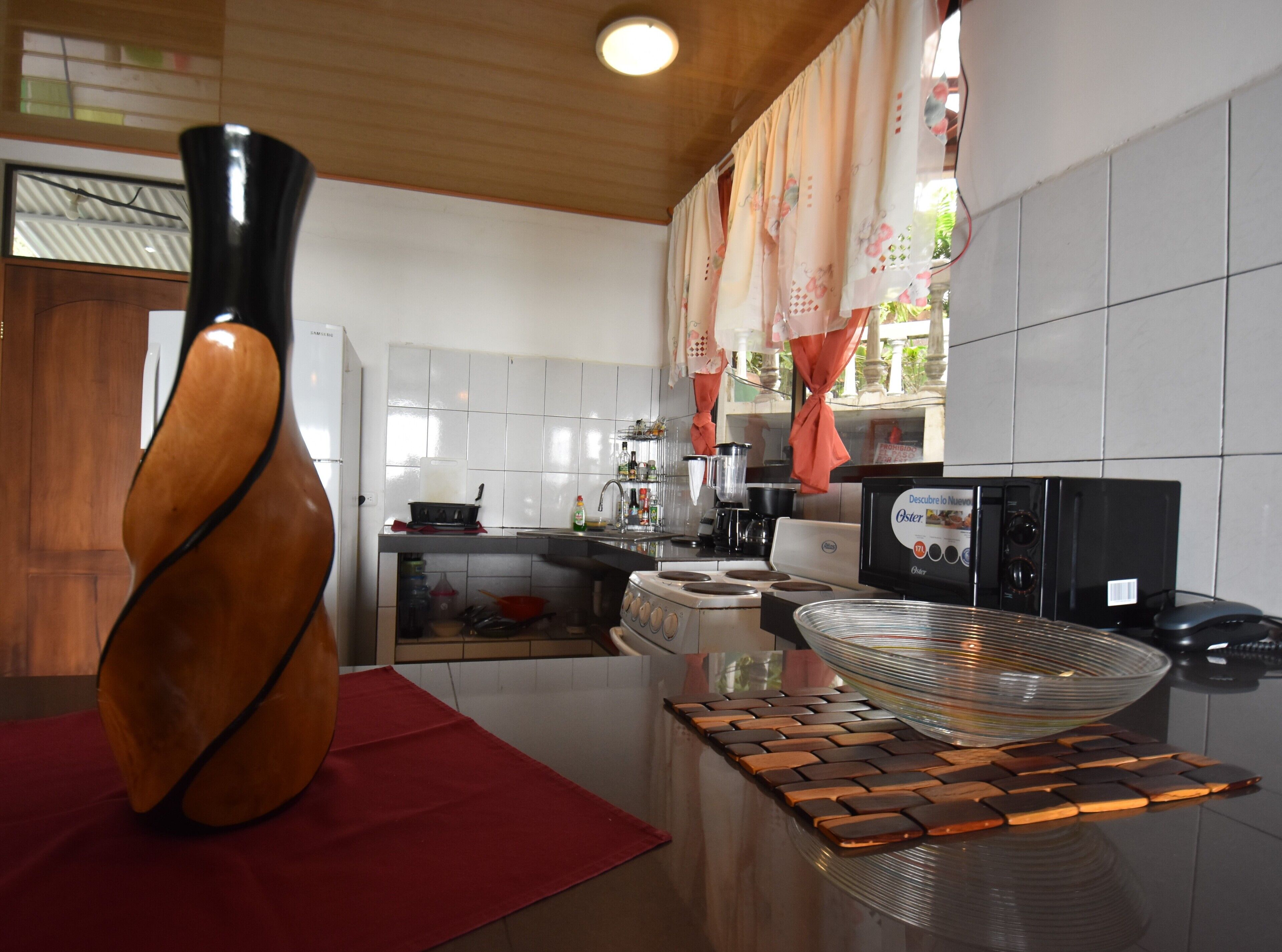 Una cocina moderna con un jarrón de madera, una cafetera y un bol de vidrio grande sobre una superficie reflectante.