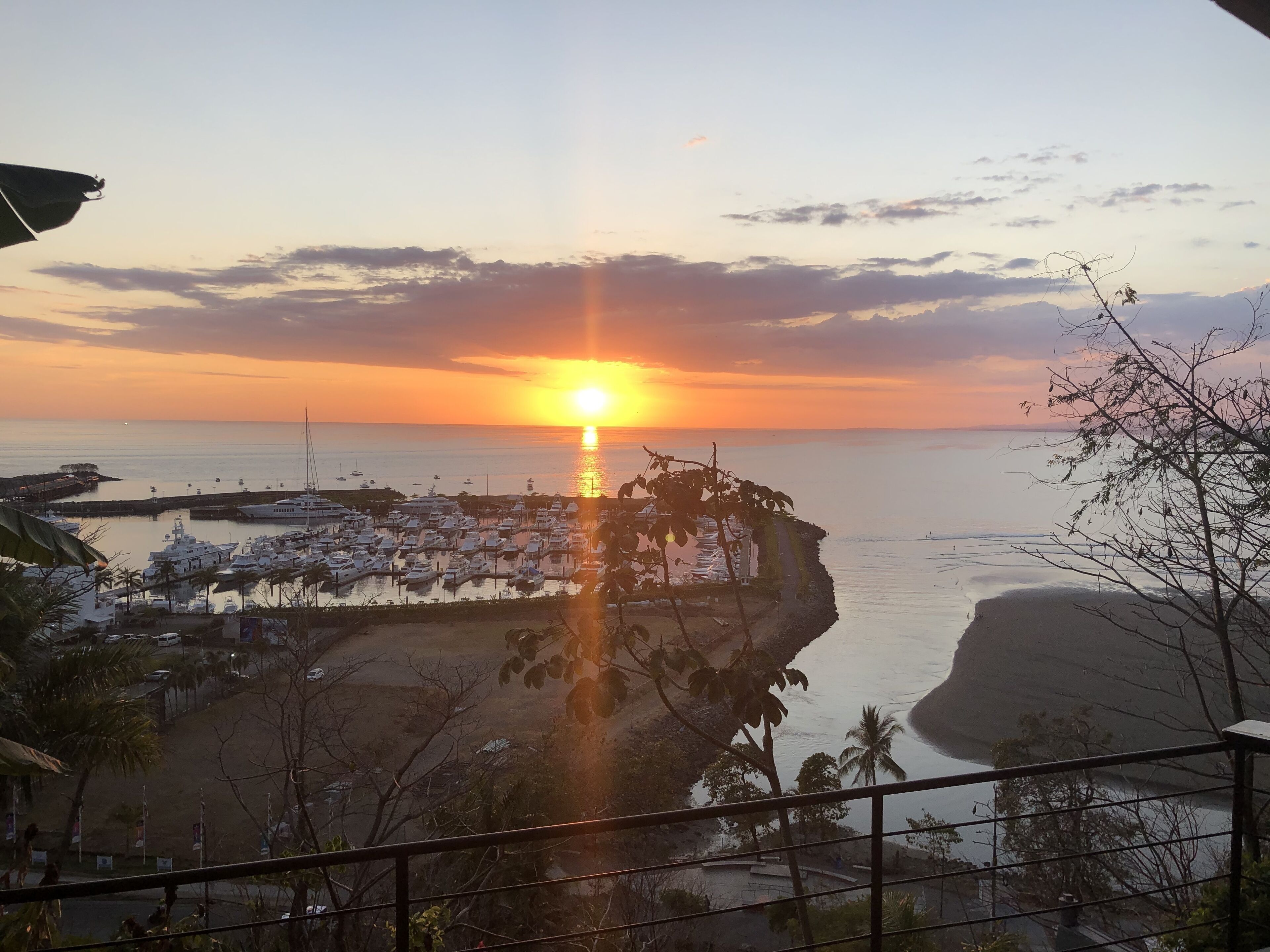 A marina with boats docked, a sunset in the background, and a view of the coastline.