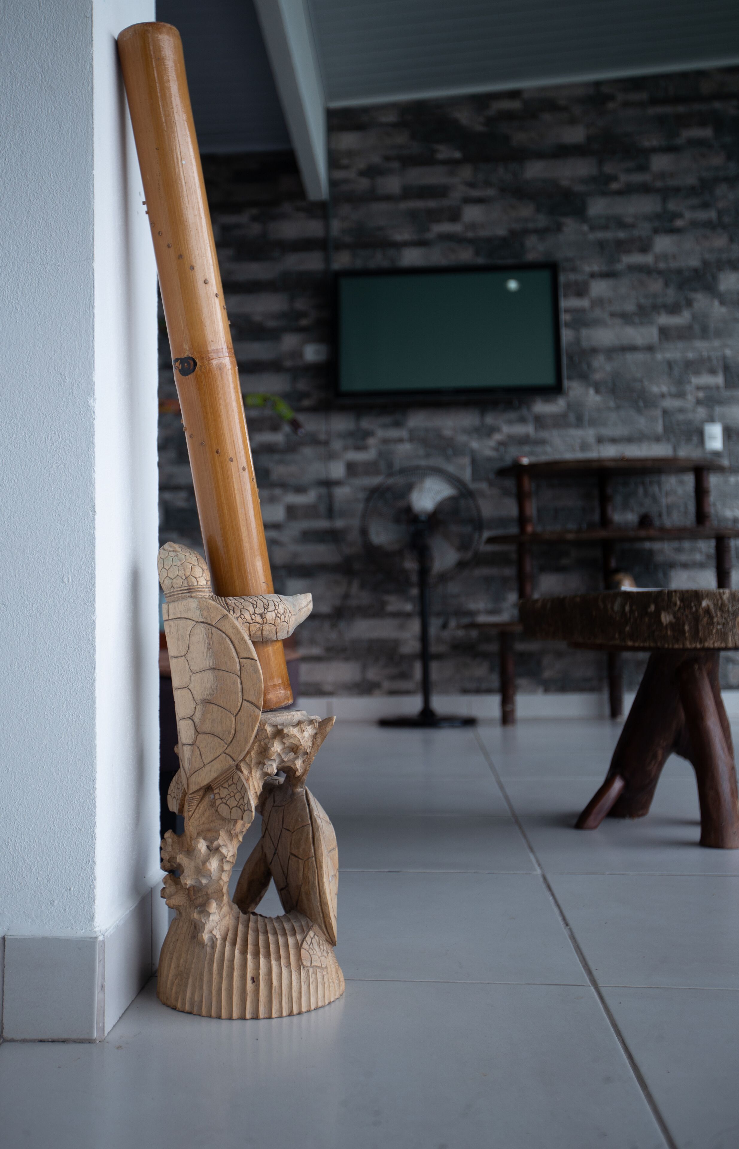 A room with a stone wall, a wooden floor, a television mounted on the wall, and a wooden table with chairs.