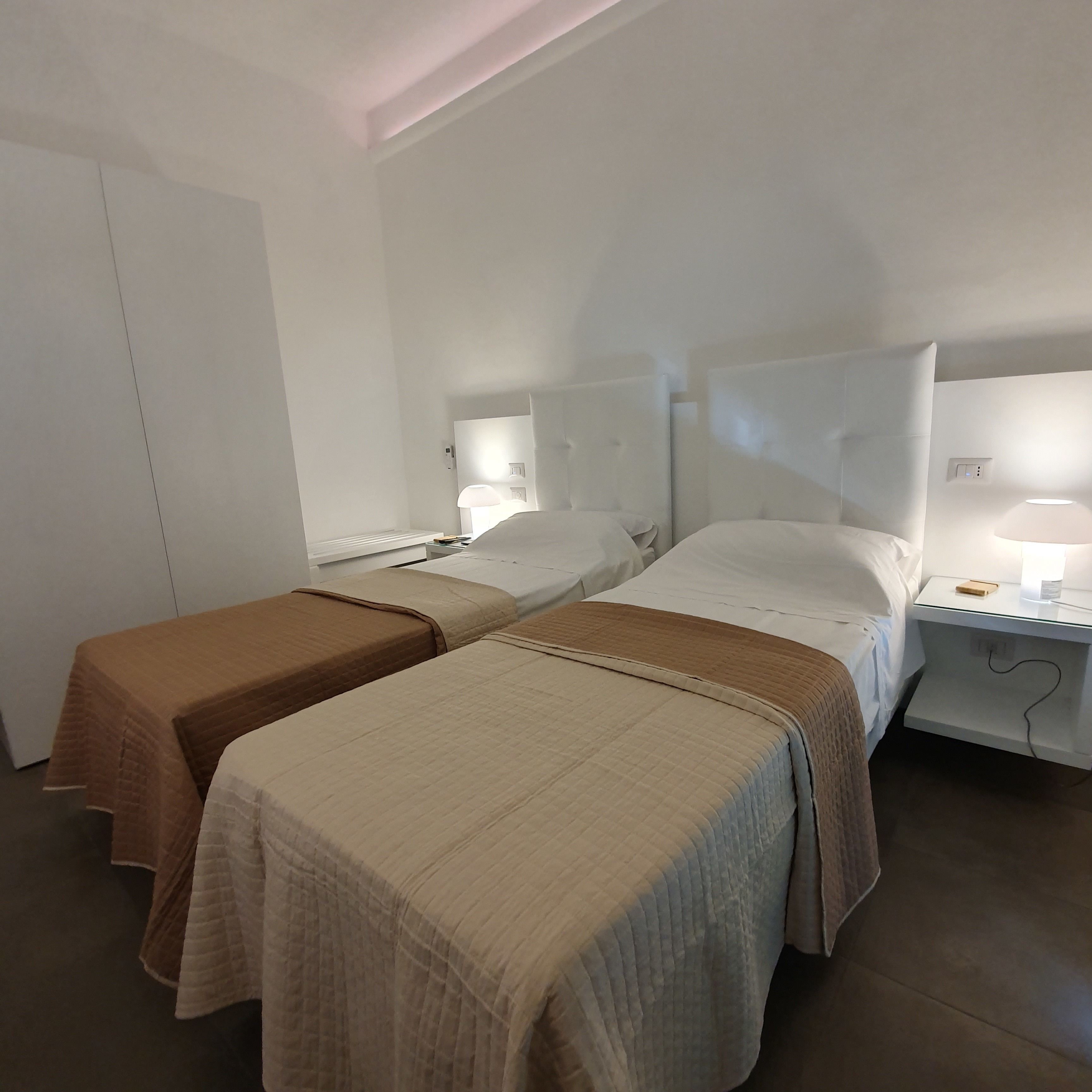 Una habitación de hotel con dos camas, una mesita de noche con lámpara y una puerta.