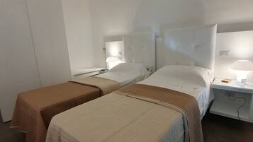 Una habitación de hotel con dos camas, una mesita de noche con lámpara y una puerta.