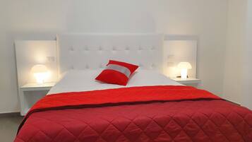 Ein Bett mit einer roten gesteppten Tagesdecke und einem roten Kopfkissen, an beiden Seiten zwei Nachttische mit Lampen.
