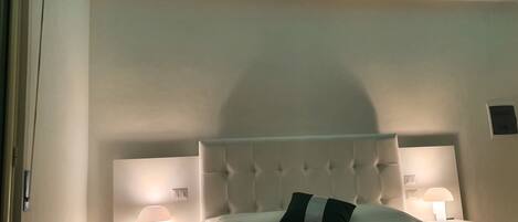 A neatly made bed with a green quilt, two bedside lamps, and a ceiling light strip.