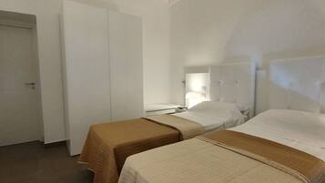 Two single beds with brown headboards and quilted bedspreads, a nightstand with a lamp, and a small table between.