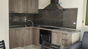 A modern kitchen with dark wood cabinets, a black stove, and a built-in dishwasher. - Fantasia B&B (Reggio Calabria)