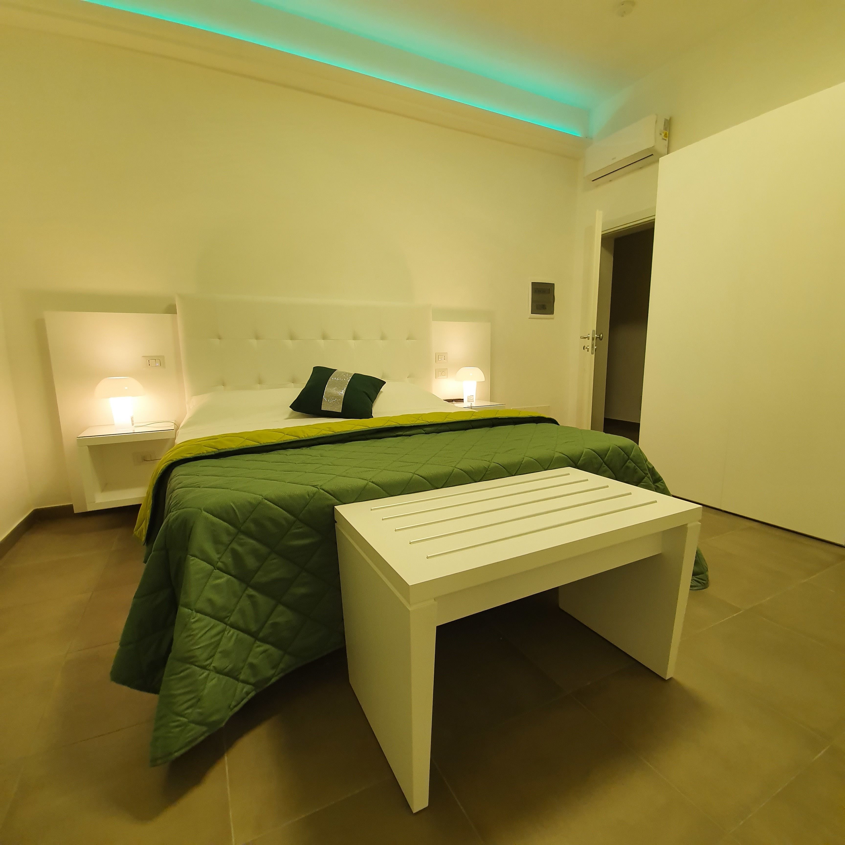 Een netjes ingerichte slaapkamer met een bed, bedlampjes, een nachtkastje en een bankje.