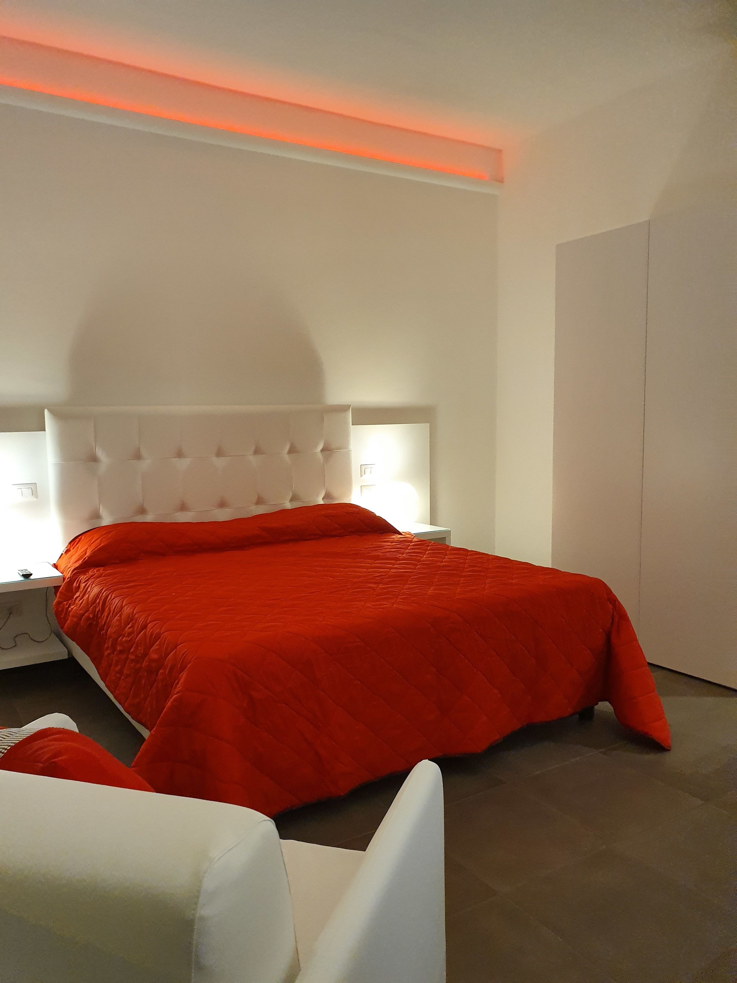 A modern bedroom with a large bed, white headboard, and a red bedspread.