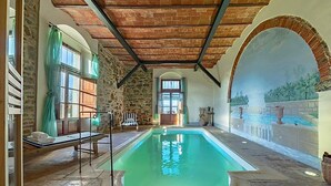 Une piscine dont le fond est en pierre, avec un banc et une fresque représentant un paysage.
