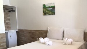 Una camera d'hotel con un letto, cuscini bianchi, un piccolo frigorifero e un quadro appeso al muro.