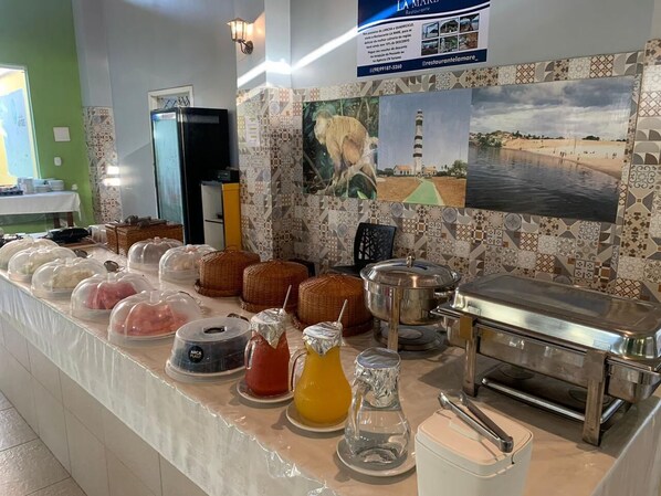 Een buffetopstelling met afgedekte gerechten, een drankstation en een koelkast.