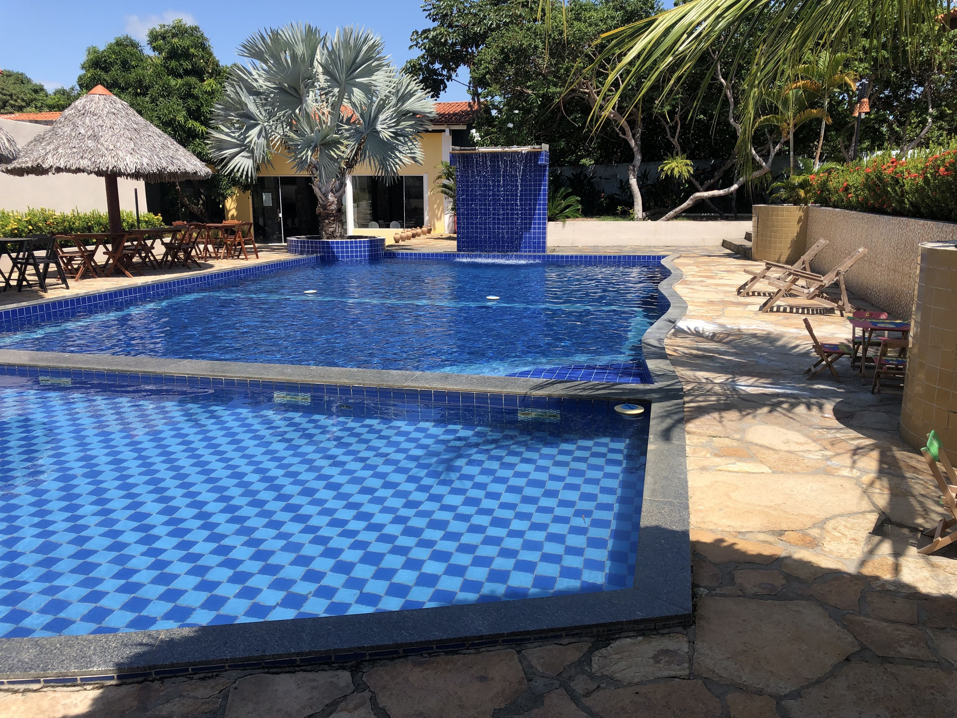 Una piscina con diseño de tablero de ajedrez, rodeada de sillas de descanso y una palmera.