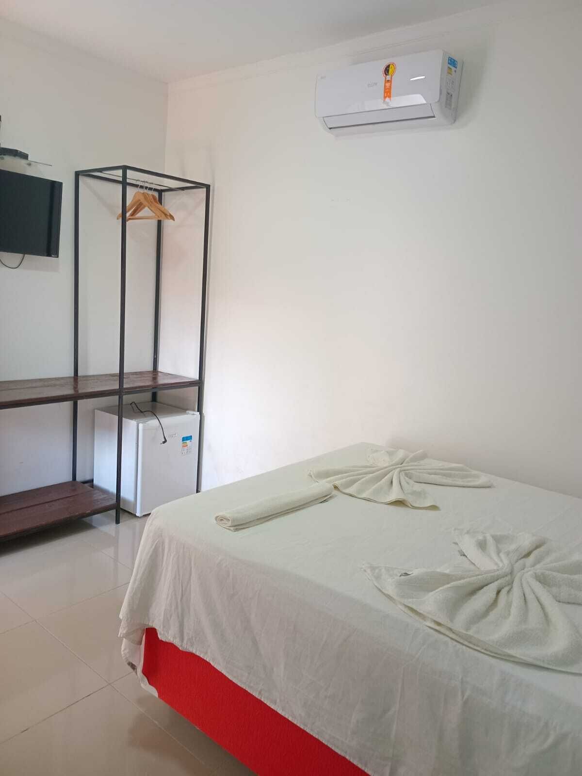 Habitación de hotel con cama, televisión, armario y un pequeño refrigerador.