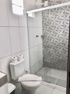 A modern bathroom with a toilet, a shower with a geometric tile pattern, and a toilet paper holder. - Pousada Recanto das Arvores (Barreirinhas)