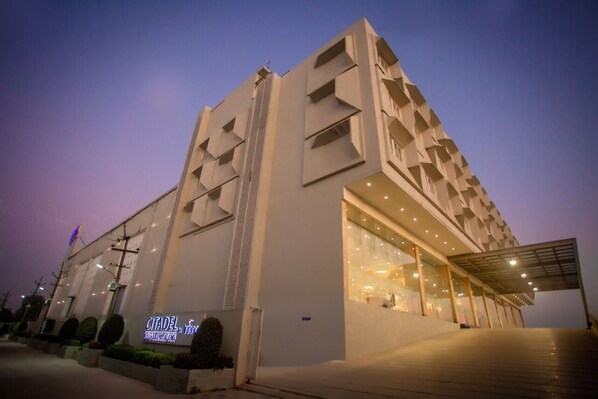 A modern building with a unique geometric facade, a prominent entrance with glass doors, and a sign indicating it is a hotel. - CITADEL Hotel By Vinnca (Hyderabad)