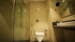 A modern bathroom with a glass-enclosed shower, a toilet, and a vanity with a mirror and a small plant. - CITADEL Hotel By Vinnca (Hyderabad)