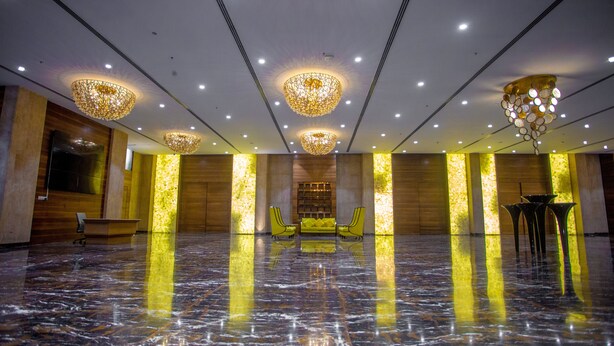 A spacious lobby with a reflective marble floor, a central seating area with yellow chairs, and multiple chandeliers. - CITADEL Hotel By Vinnca (Hyderabad)
