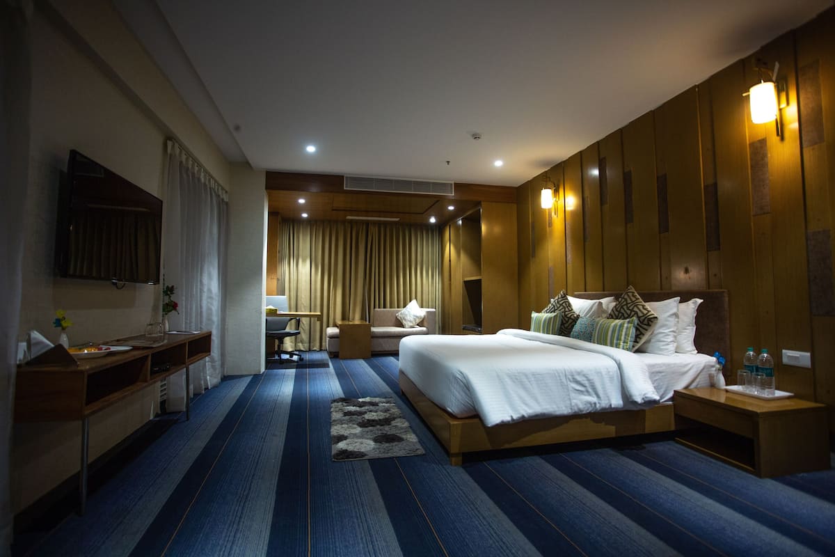 A hotel room with a large bed, a desk, a chair, and a TV mounted on the wall.