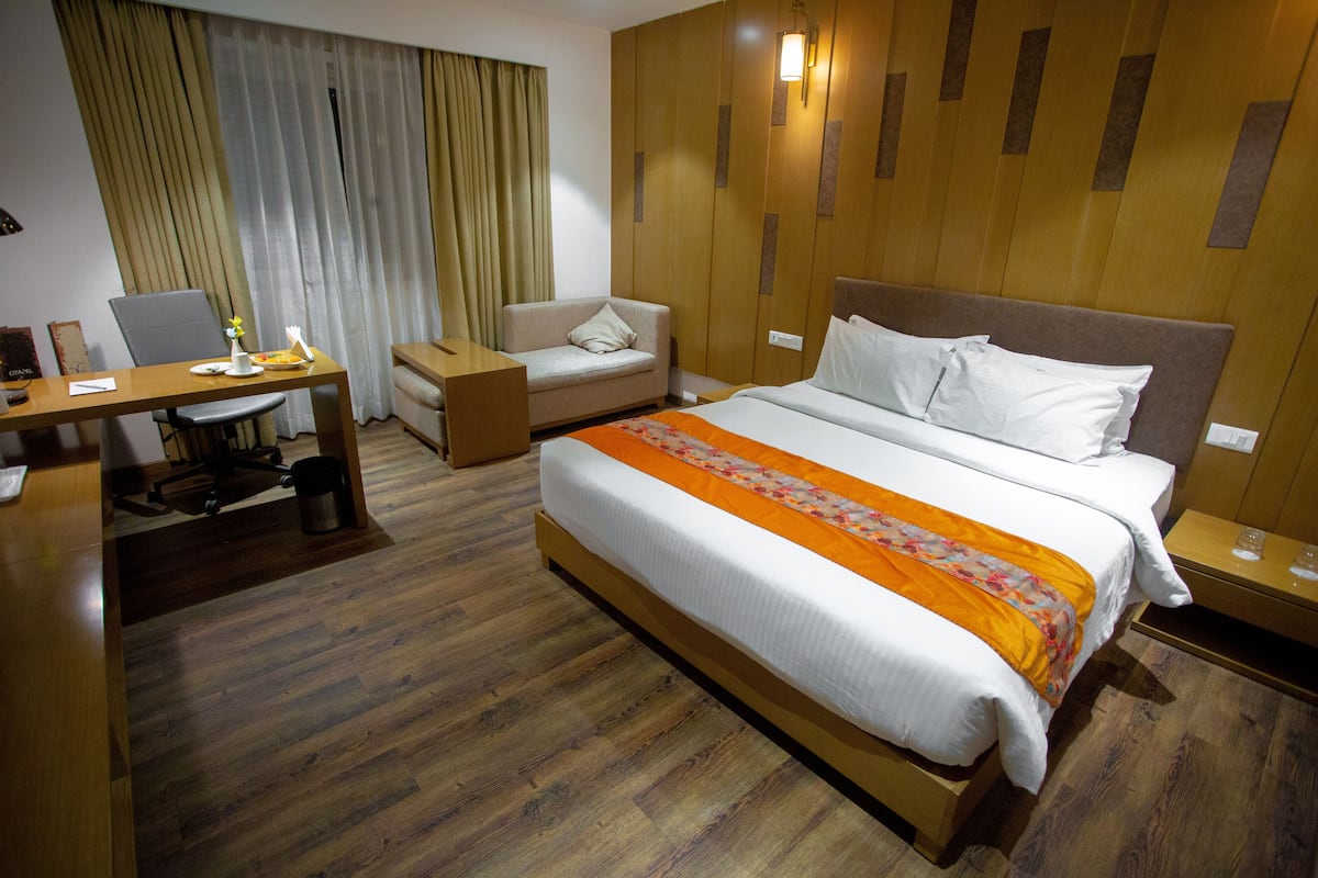 A hotel room with a large bed, a desk, a chair, a sofa, and a wardrobe.