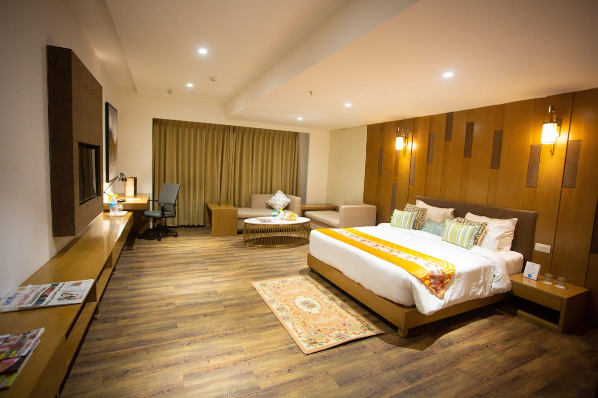 A hotel room with a large bed, a desk with a chair, a sofa, and a small table.