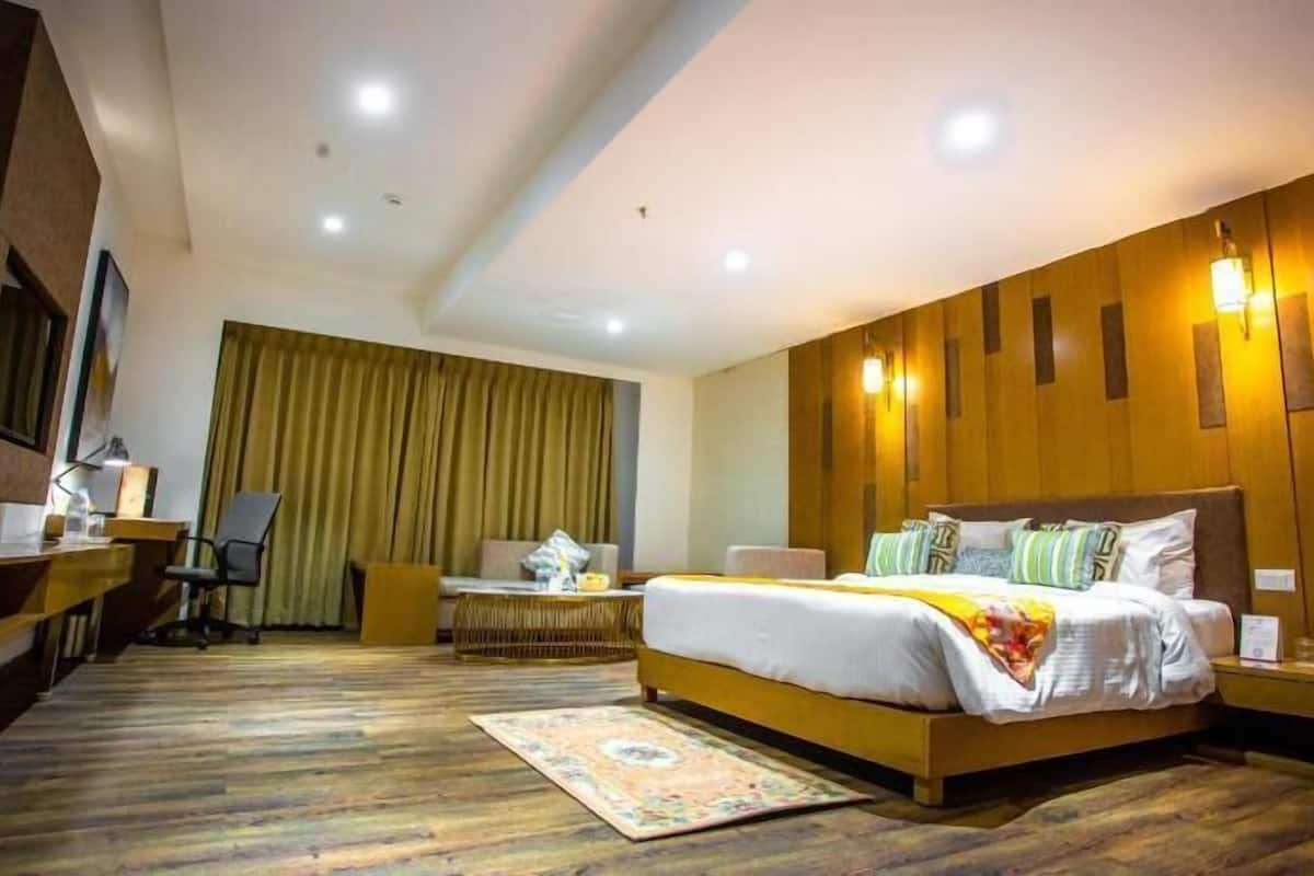 A hotel room with a large bed, a desk, a chair, a desk lamp, and a window with curtains.