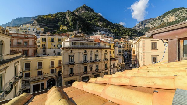 Un pueblo costero con edificios en una ladera, cielo despejado y una montaña al fondo.