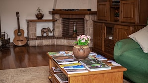 Una sala de estar con una mesa de centro de madera que sostiene revistas de viajes, un florero con flores, una guitarra y una chimenea.