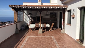 Un patio techado con una mesa y sillas de comedor, una zona de cocina y vistas al mar.