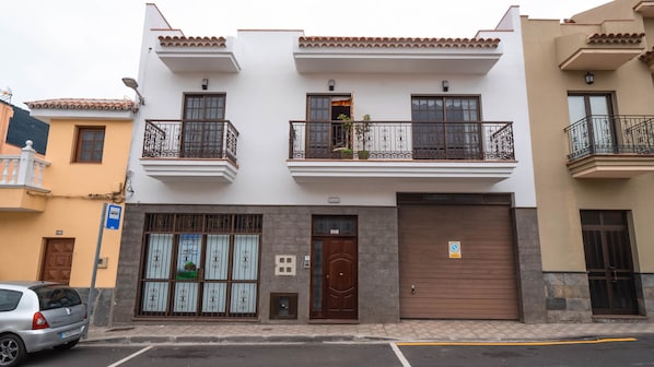 A two-story building with a garage door, a balcony with iron railings, and a small window with a plant.
