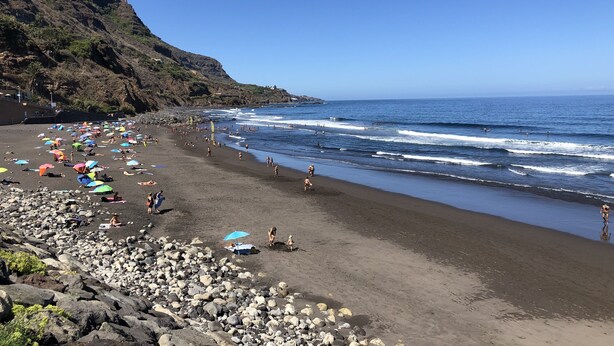 Una playa con terreno rocoso, sombrillas y gente.