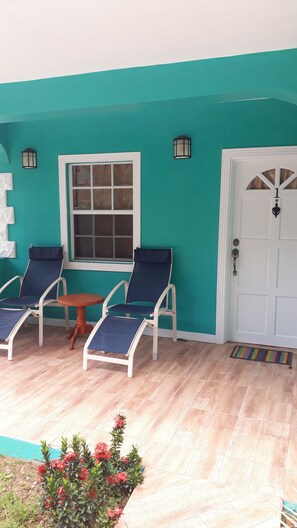 A turquoise-painted exterior of a house with a white door, a window, and two blue lounge chairs. - Amazon Villas (Soufrière)