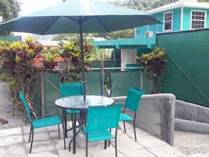 A patio area with a round table and four chairs, an umbrella, and potted plants. - Amazon Villas (Soufrière)