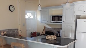 Una cocina con una isla central, sillas de madera, microondas y refrigerador.